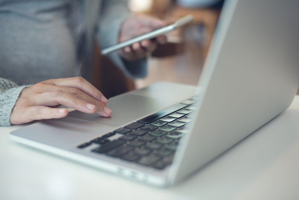 A woman sitting at a desk with a laptop and her smartphone shopping on social media