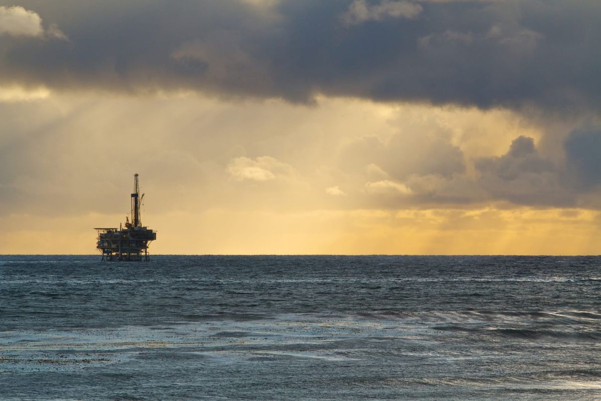 Dark ominous storm cloud with distant rain over the ocean with an offshore oil derrick drilling rig pump in the distance.