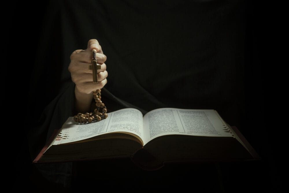 Closeup of Hands holding rosary beads and cross while reading bible