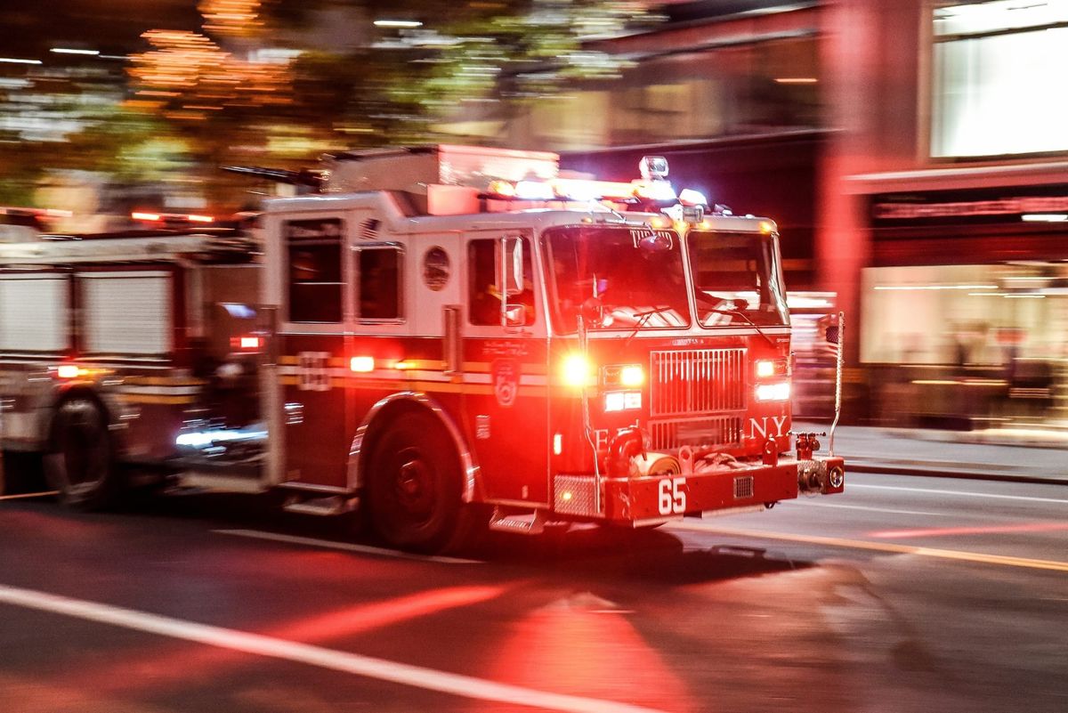 Fire truck with emergency lights racing to the scene of a fire on a city street.