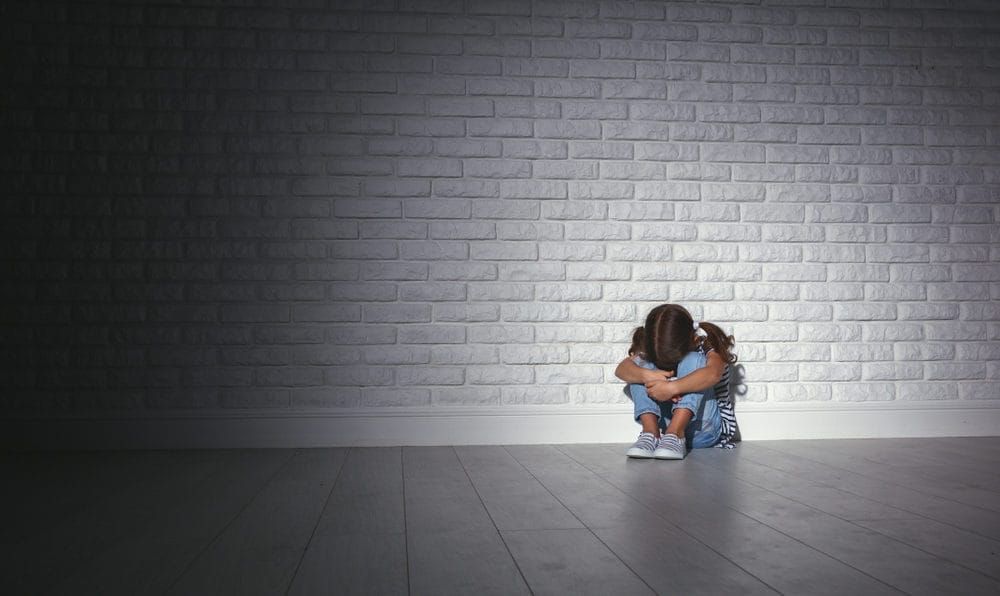 Upset sad sad child girl in stress sits and cries at an empty dark wall